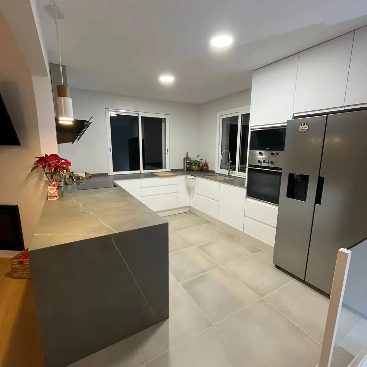 Cocina blanca con península de piedra gris, frigorífico americano, horno integrado y suelo de gres